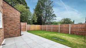 Un jardin avec un mur en briques, une clôture en bois et une pelouse verdoyante.