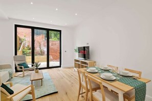 A modern living room with a dining area, a TV, and a sliding glass door leading to a brick exterior. - 3Bd Home, Relocations Long Stays Families Workers (Greater London)