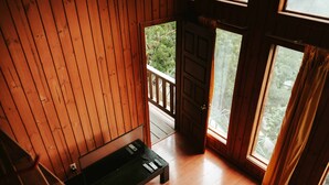 A wooden interior with a bench, a door leading outside, and a window with curtains.