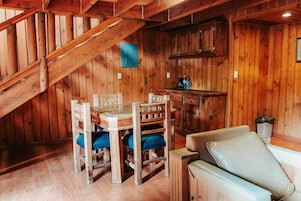 A wooden interior with a dining table and chairs, a sofa, and a kitchenette area.