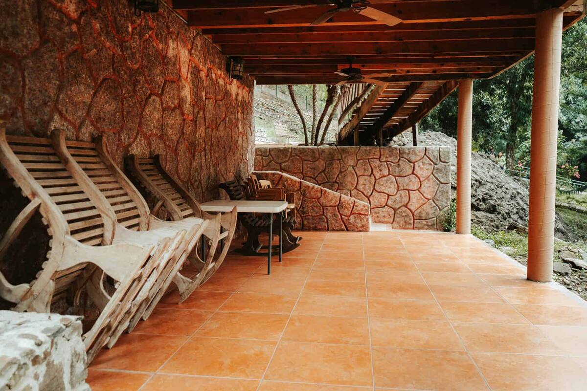 Un patio al aire libre con paredes de piedra, mobiliario de madera y un ventilador de techo.