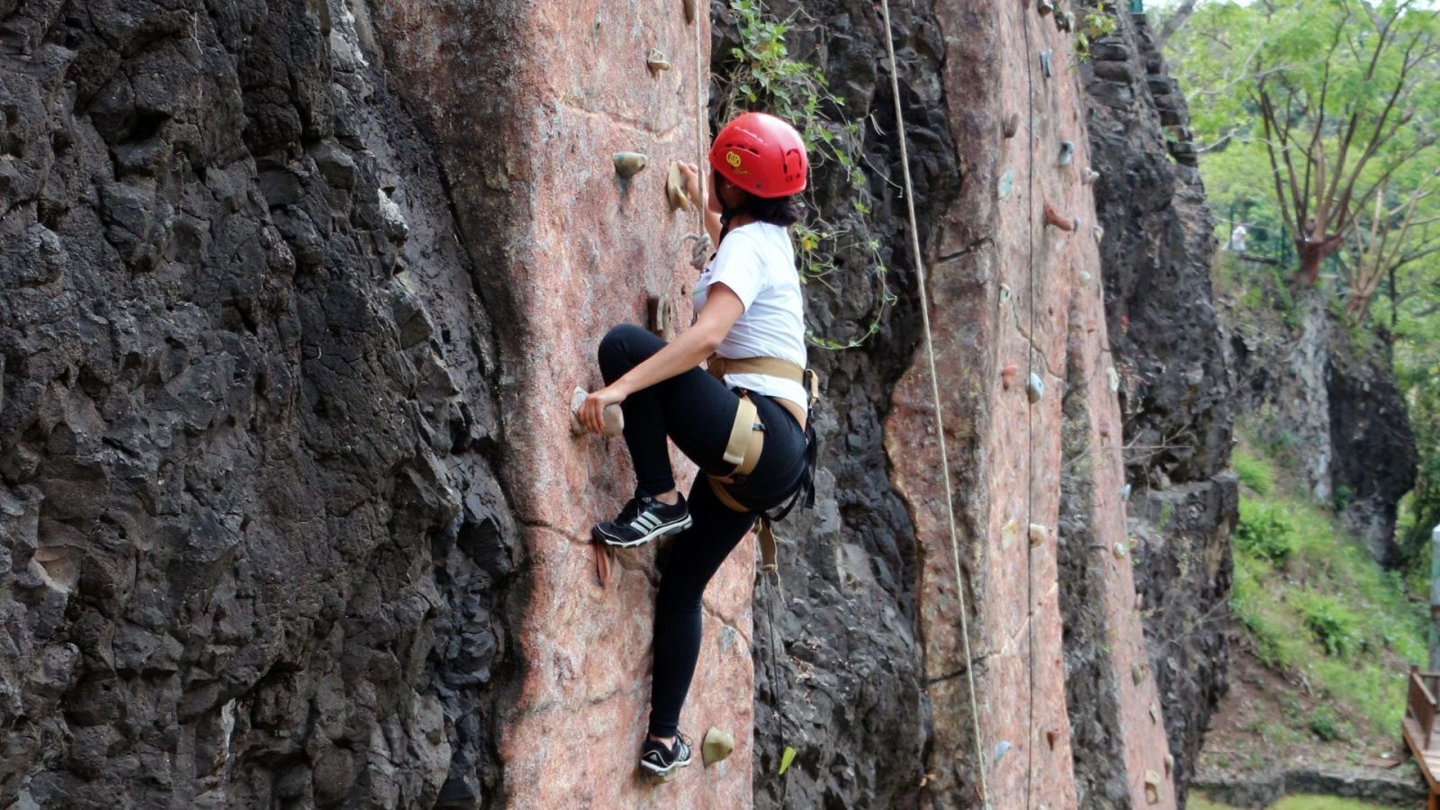 Eine Person besteigt einen felsigen Klippenhang mit Klettergurt und Helm.