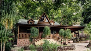 A wooden cabin with a stone foundation, a staircase leading to the entrance, and a garden with various plants.