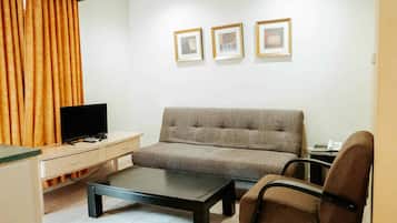 Una sala de estar con sofá, mesa de centro, televisor y escritorio. Hay tres cuadros enmarcados en la pared.