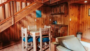 Un interior de madera con una mesa de comedor, sillas, un sofá y una zona de cocina.