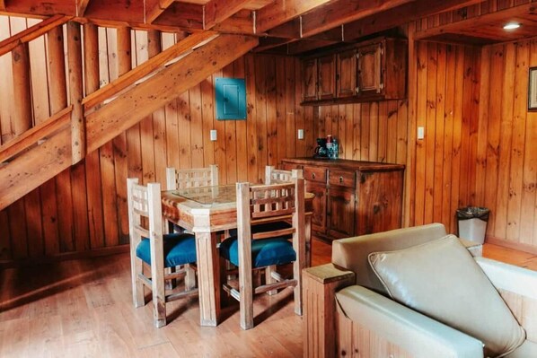 Een houten interieur met een eettafel, stoelen, een bank en een keukenhoek.