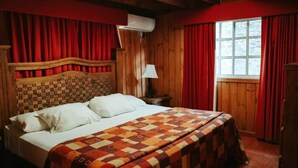 Una habitación de madera con una cama, cortinas rojas, una ventana y una lámpara.