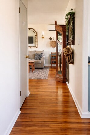 A hallway with a wooden floor leading to a living room with a sofa, a small table, and a lamp.