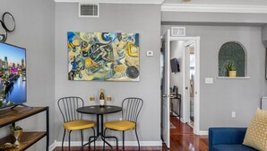 A living room with a TV, two chairs, a table with a bottle and glasses, a colorful abstract painting, and a blue sofa. - Urban Retreat • Explore DTSP, Walk Everywhere! (St. Petersburg)