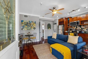 A modern living room with a blue sofa, a dining area with chairs, a kitchen with wooden cabinets, and a ceiling fan. - Urban Retreat • Explore DTSP, Walk Everywhere! (St. Petersburg)