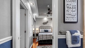 A hallway leading to a bedroom with a bed, a ceiling fan, and a wall-mounted sign with hygiene instructions. - Urban Retreat • Explore DTSP, Walk Everywhere! (St. Petersburg)