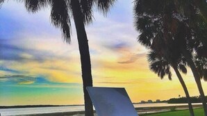 A beachside setting with a table, a bottle of wine, and a glass, set against a sunset backdrop. - Urban Retreat • Explore DTSP, Walk Everywhere! (St. Petersburg)