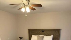 Un dormitorio con cama de madera, ventilador de techo y mesita de noche con lámpara.