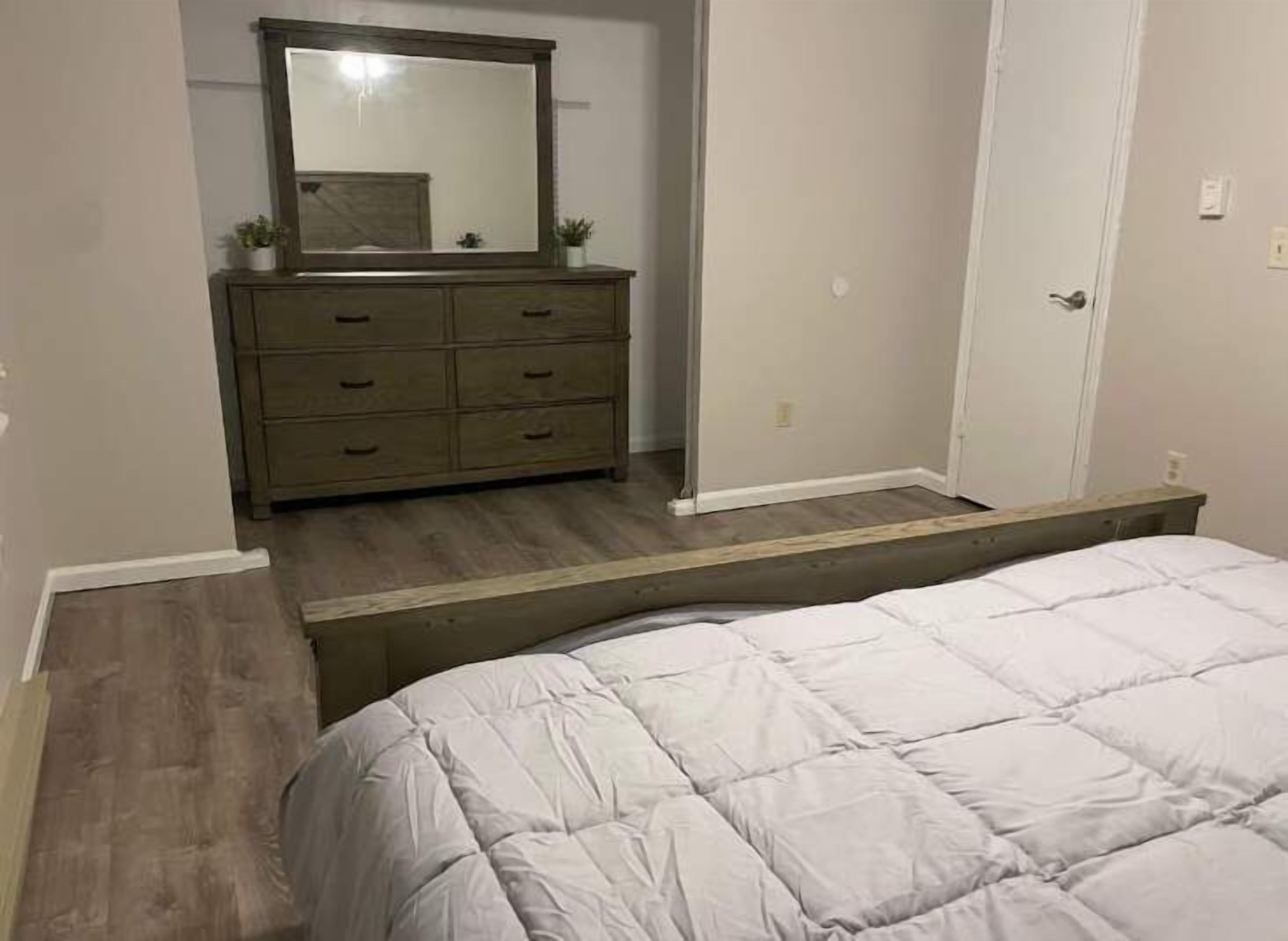 A bedroom with a bed, a dresser, a mirror, and a door.