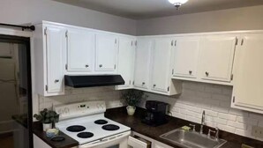 Una cocina con armarios blancos, una estufa, un fregadero y una encimera negra.