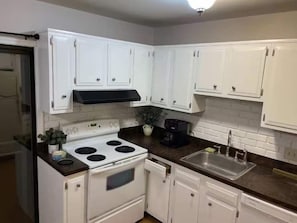 A kitchen with white cabinets, a stove, a sink, and a black countertop.