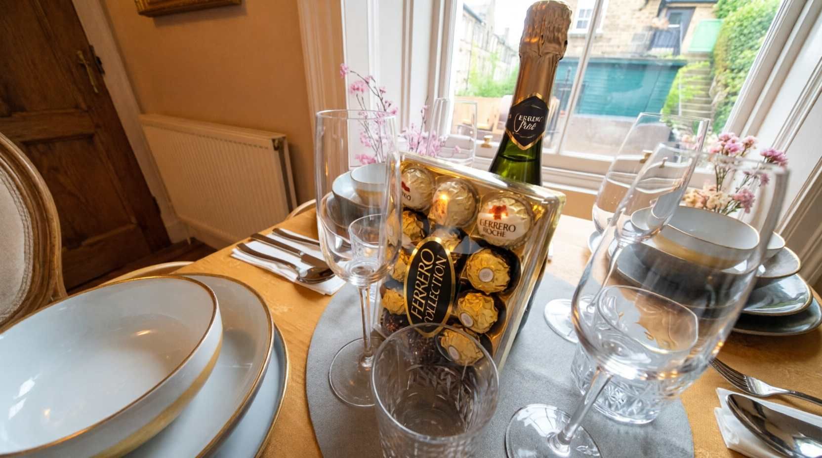 Ein gedeckter Tisch mit Tellern, Besteck, Gläsern, einer Champagnerflasche und einer Schachtel Ferrero Rocher Pralinen.