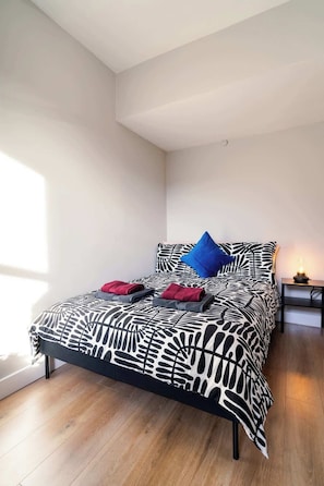 A bedroom with a bed, pillows, a bedside table, and a lamp.