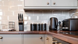 Cozinha com design moderno, destacando um balcão de madeira, uma máquina de café e recipientes pretos identificados com tipos de bebida.