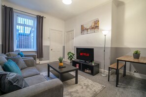 Een moderne woonkamer met een bank, salontafel, televisie en een schilderij aan de muur.