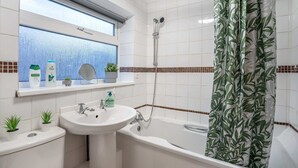 Ett badrum med ett vitt handfat, en spegel, en dusch och ett fönster med utsikt.