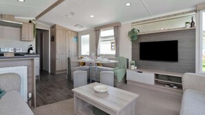 Una sala moderna con televisor de pantalla plana, una zona de comedor con una mesa redonda y una cocina con armarios de madera.