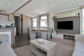 Ein modernes Wohnzimmer mit Flachbildfernseher, ein Essbereich mit rundem Tisch und eine Küche mit Holzausbau.