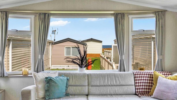 Una habitación con sofá, planta en maceta y vistas a casas vecinas a través de amplios ventanales.