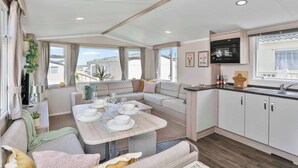 Interior moderno de autocaravana con comedor, sofá, cocina y ventanas amplias.