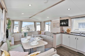 Ein modernes Wohnmobil-Interieur mit Essbereich, Sofa, Küche und großen Fenstern.