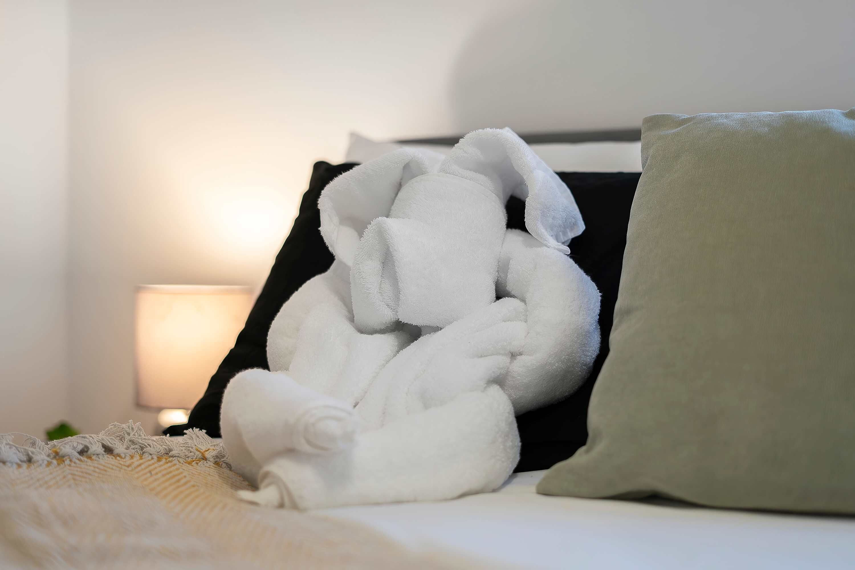 A neatly made bed with a white blanket and a green pillow.