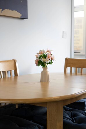 A round wooden table with a vase of flowers, two wooden chairs, and a plain white wall with a window. - Nr Durham - Free Parking- 2BR Home- Wi-Fi-Sleeps 5 (Coxhoe)