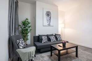 A modern living room with a grey sofa, a black coffee table, a grey armchair, a potted plant, and a framed tiger artwork on the wall.