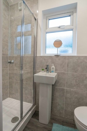 A bathroom with a glass-enclosed shower, a pedestal sink, and a window above the mirror.