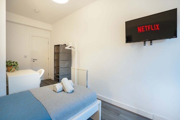 Una habitación de hotel moderna con una cama, un televisor montado en la pared, una mesita de noche y un radiador.