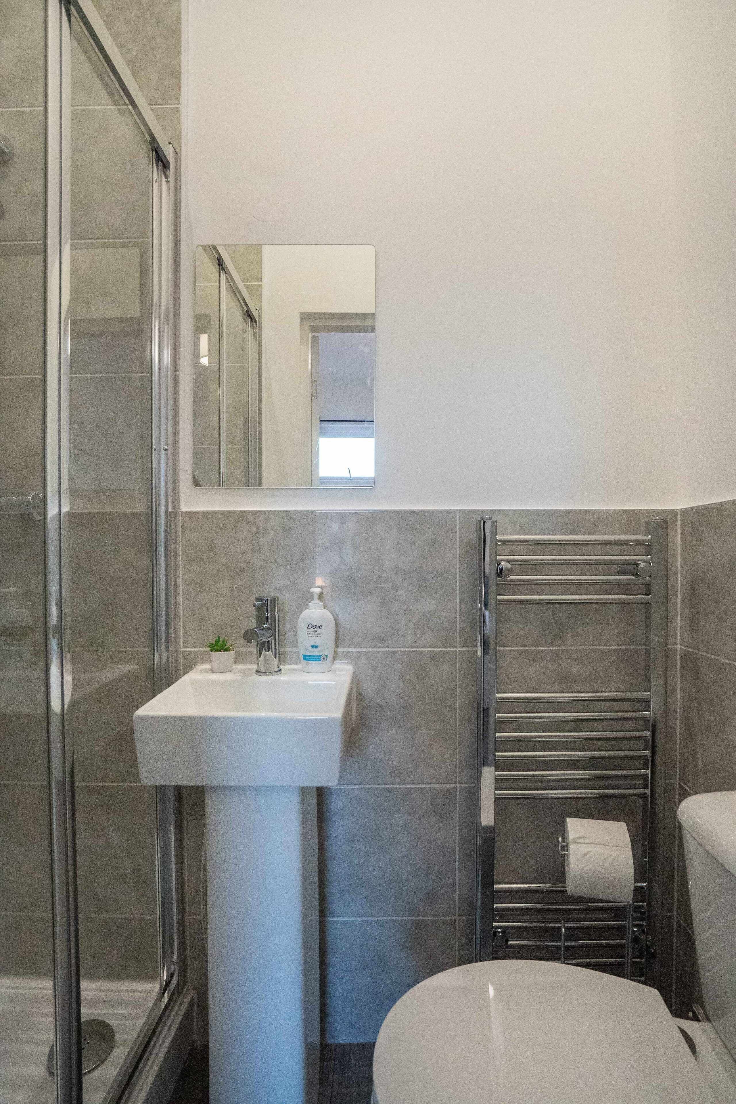 Un baño con cabina de ducha de vidrio, lavamanos pedestal, toallero y un inodoro.