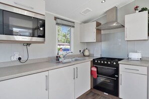 A modern kitchen with a built-in microwave, stove, oven, and a window with a view of the outside. - Seton Sands 3BR Spacious Caravan near Edinburgh (Port Seton)