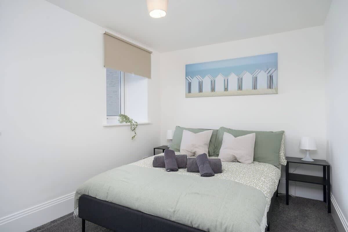 Een slaapkamer met een bed, een raam met uitzicht, een schilderij aan de muur en een nachtkastje met een lamp.