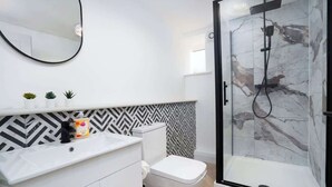 Een moderne badkamer met een douchecabine, toilet, wastafel met spiegel en een decoratieve spatwand.