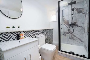 Ein modernes Badezimmer mit Duschkabine, Toilette, Waschtisch und Spiegel sowie einer gemusterten Rückwand.