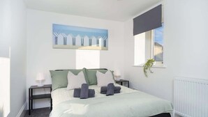 Een slaapkamer met een bed, nachtkastje, raam en een schilderij.