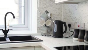 Een keuken met een zwarte waterkoker, een spoelbak en een mokkenhouder.