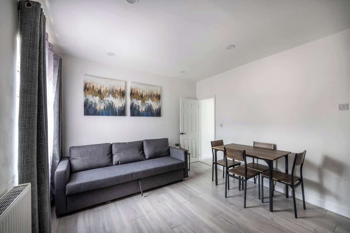 A modern living room with a grey sofa, a wooden dining table with chairs, and two abstract paintings on the wall.
