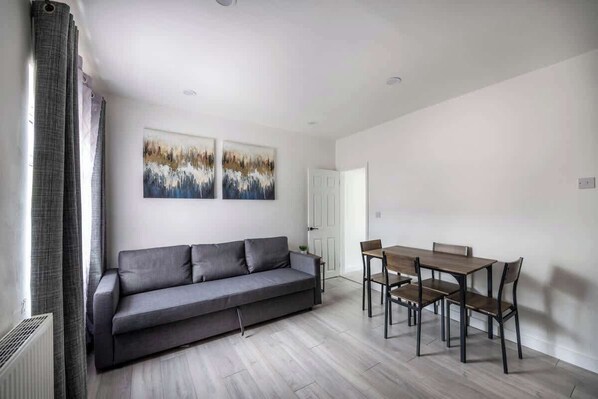 A modern living room with a grey sofa, a wooden dining table with chairs, and two abstract paintings on the wall.