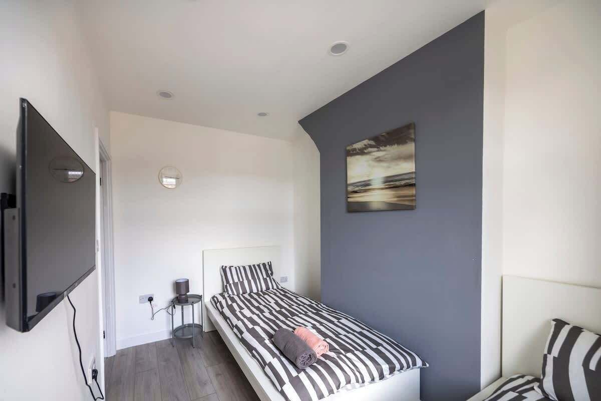 A modern bedroom with a bed, a flat-screen TV, a small bedside table, and a wall-mounted artwork.