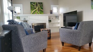 Ein Wohnzimmer mit Kamin, Fernseher und zwei grauen Sesseln.