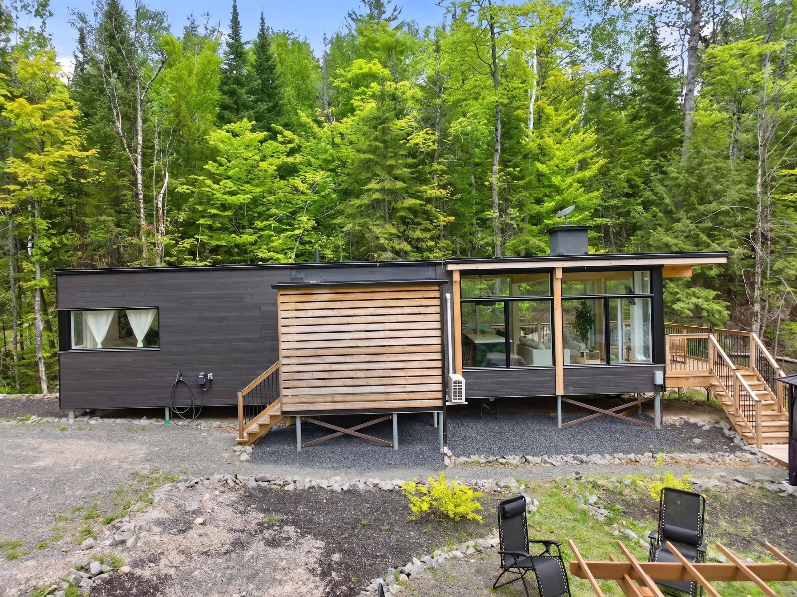 Uma cabana moderna com varanda, um espaço de estar pequeno ao ar livre e um cenário de floresta.