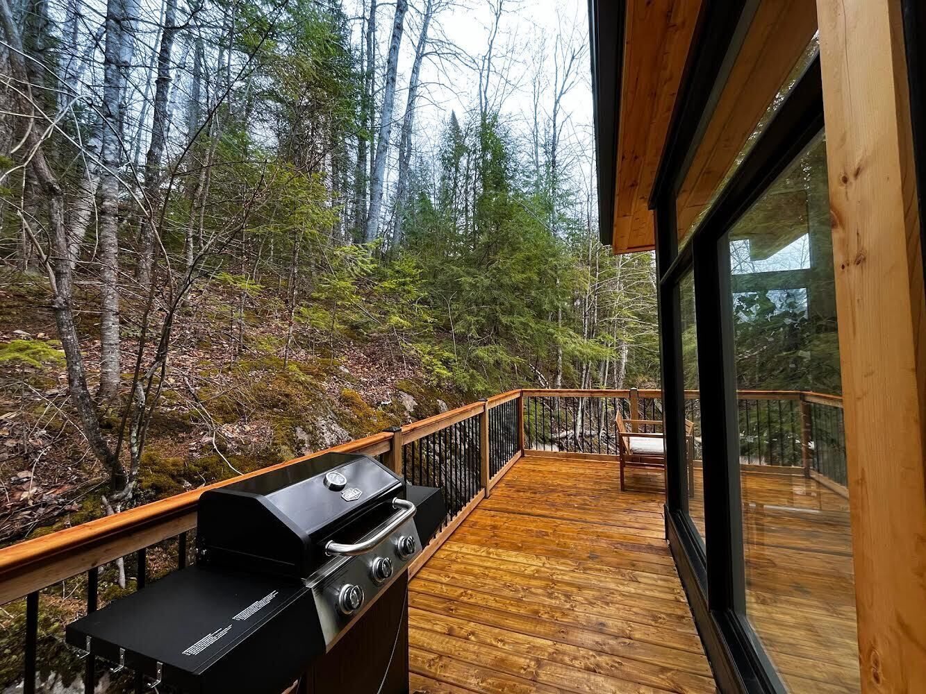 A deck with a grill, surrounded by a forest.