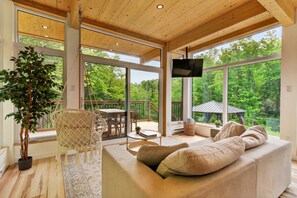 Amplia sala de estar con un sofá grande, una mesa de comedor y vistas a un bosque a través de ventanas amplias.