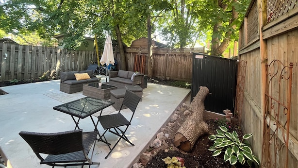 A backyard patio with a sofa, chairs, a glass table, and a wooden fence.